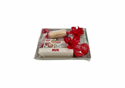 Canastilla de regalo MomentosGourmet para recién nacido con productos NUK, envuelta en celofán con lazo rojo.