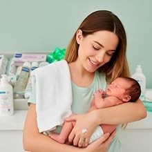 Madre sosteniendo a su bebé recién nacido junto a la canastilla de regalo MomentosGourmet con productos Mustela y Suavinex