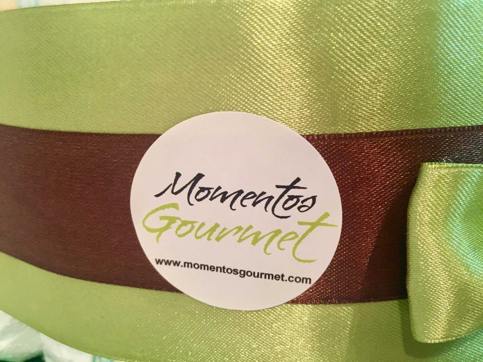 Detalle de lazo verde y marrón con pegatina de la marca MomentosGourmet en una tarta de pañales de regalo